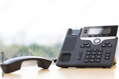 Black IP Phone on wooden table , Telephone on desk with big window city view.Modern office concept. photo