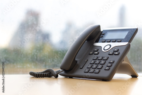 Black IP Phone on wooden table , Telephone on desk with big window city view.Modern office concept.