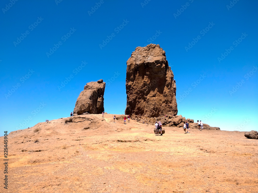 Fototapeta premium iconic famous mountain called Roque Nublo in Canary Islands Spain with people trekking in a clear blue day of summer