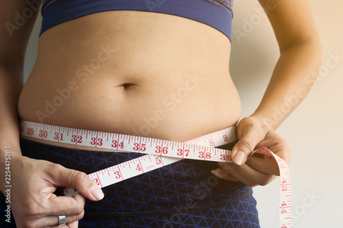 Woman hand holding measuring tape on belly fat