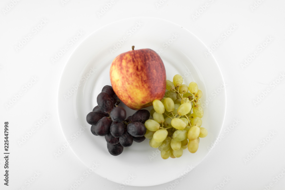 vegetarian diet: still life from different grapes and ripe Apple on a white plate. white background vegetarian diet: still life from different grapes and ripe Apple on a white plate. white background
