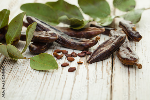 Carob. Healthy organic sweet carob pods with seeds and green leaves on a wooden board. Healthy eating, food background.