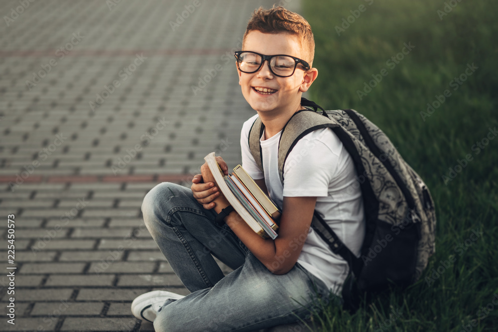 Obraz premium Portrait of a Little Boy in White T-Shirt and Jeans Holding Books in Hands Outdoors