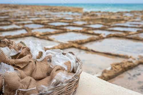 Salinas. Salt Pans or salters at the background with salt bags ready for sale in a basket or bowl outdoor. Hand harvest salt in Gozo Island Marsalforn. space for text. photo