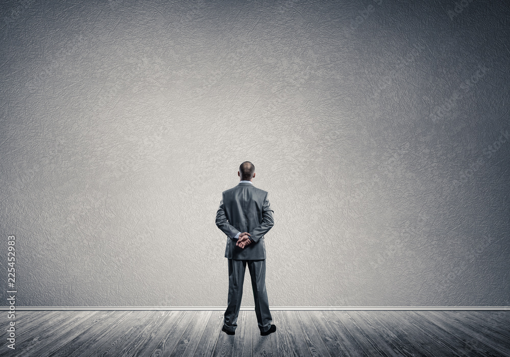 Fototapeta premium Businessman with hands behind his back and looking at blank conc