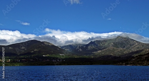 Panorámica de lago, bosques, montañas nevadas, nubes y cielo azul.