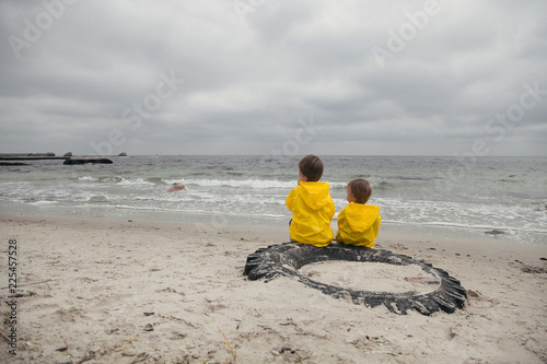 Two children in yellow clothes sit on the beach and look to one side.