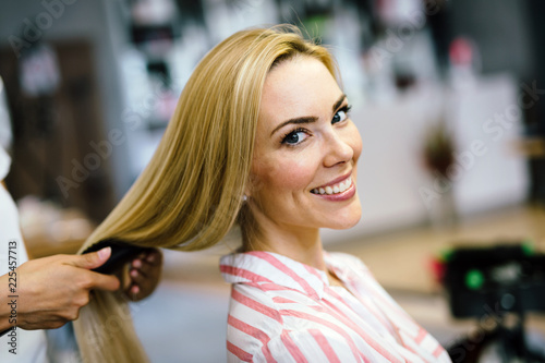 Happy young woman and hairdresser with fan making hot styling