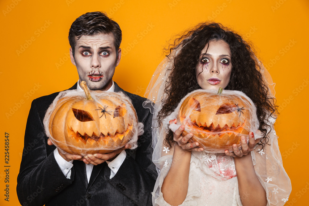 Surprised halloween bride and groom looking camera and holding pumpkin Surprised halloween bride and groom looking camera and holding pumpkin