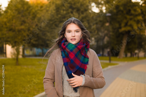 Portrait of a beautiful girl in park. Teenage girl with colorful scarf and brown coat. Close up photo. Young student have fun. Lifestyle photo. beautiful hair.