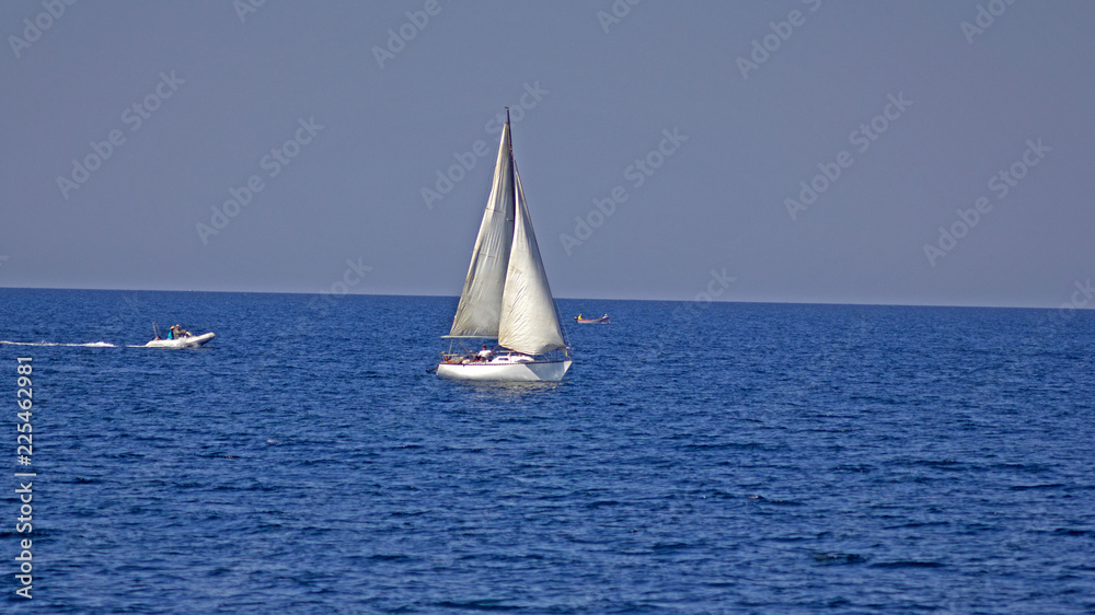 White sailboat on a background of blue sea. Sailing boat with a white sail in the blue sea in summer. 