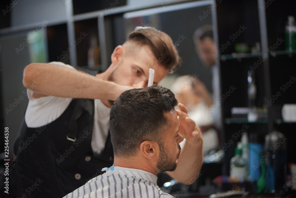 Barber styling client's hair and beard in barbershop. Barber styling client's hair and beard in barbershop.