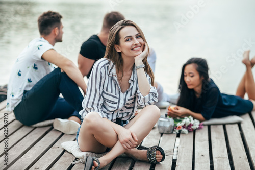 Young beautiful woman relaxing by river in company of friends