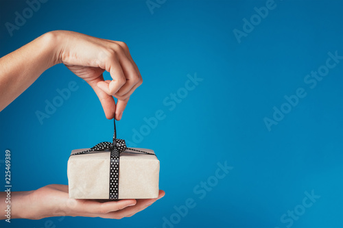 Woman hands unpacking gift box with bow on a blue background, copy space