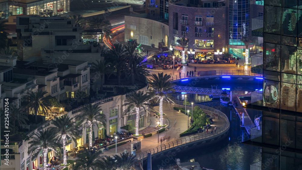 Fototapeta premium Promenade and canal in Dubai Marina with luxury skyscrapers and yachts around night timelapse, United Arab Emirates