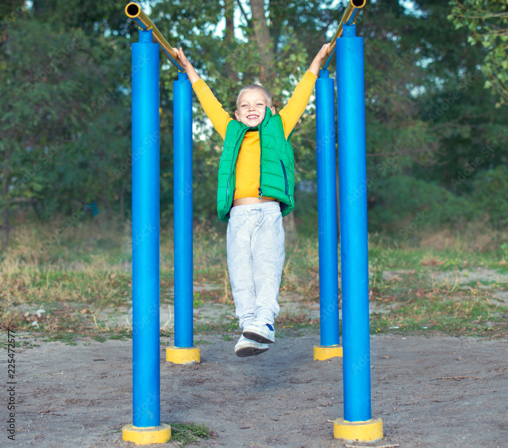 Fototapeta premium Boy athlete doing pull ups.Active lifestyle. The child performs exercises on uneven bars on the street.