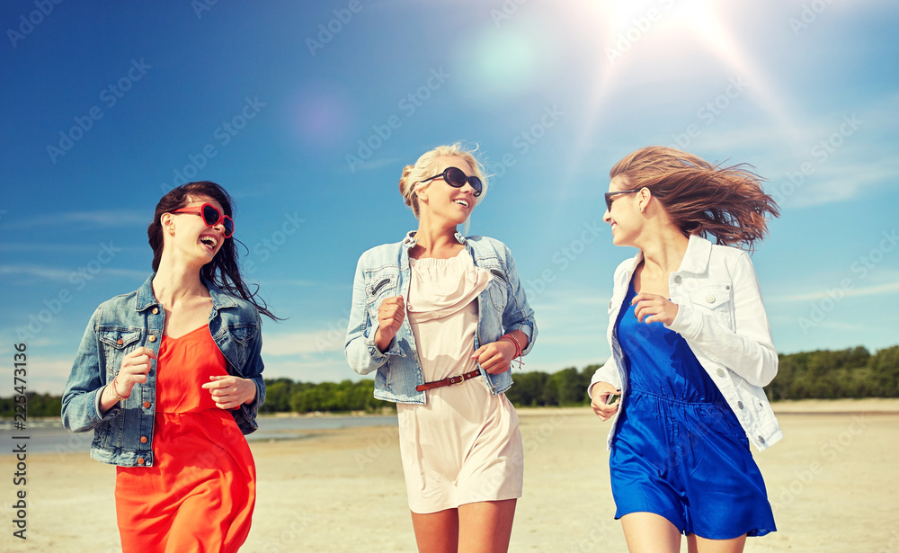 summer vacation, holidays, travel and people concept - group of smiling young women in sunglasses and casual clothes running along beach