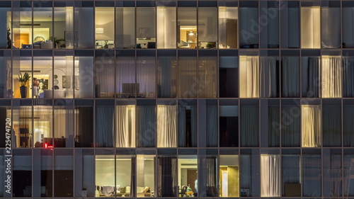 Windows of the multi-storey building of glass and steel lighting inside and moving people within timelapse