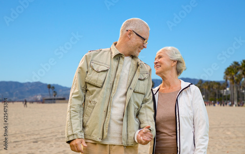 old age, travel and tourism and people concept - happy senior couple holding hands over venice beach background in california