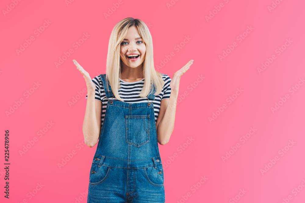 happy beautiful girl in denim overall gesturing and looking at camera isolated on pink happy beautiful girl in denim overall gesturing and looking at camera isolated on pink
