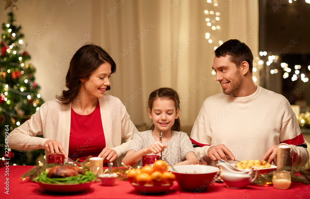 holidays, family and celebration concept - happy mother, father and little daughter having christmas dinner at home
