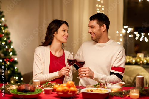 holidays, family and celebration concept - happy couple having christmas dinner at home and drinking red wine and clinking glasses