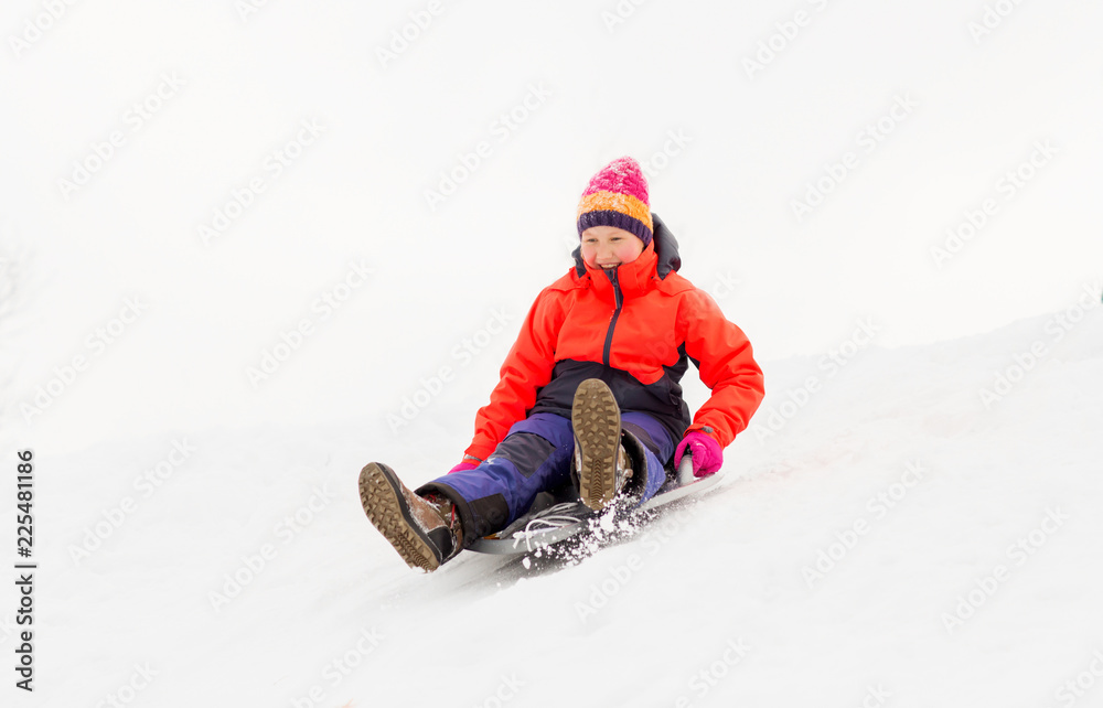 childhood, sledging and season concept - happy little girl sliding down on snow saucer sled outdoors in winter childhood, sledging and season concept - happy little girl sliding down on snow saucer sled outdoors in winter