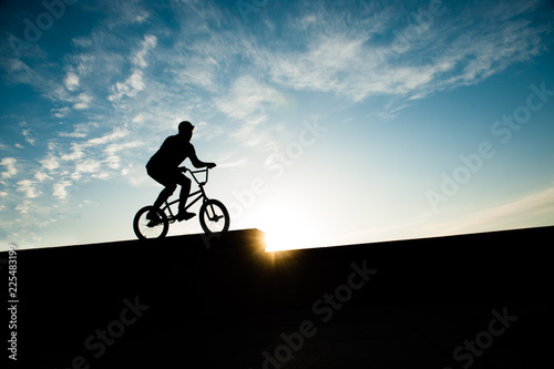 silhouette of young biker on bicycle on blue sunset sky with clouds background