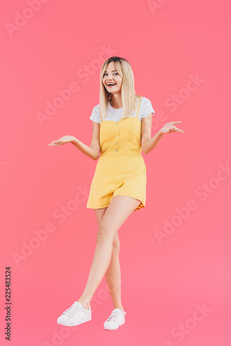 happy young stylish woman doing dubium gesture isolated on pink