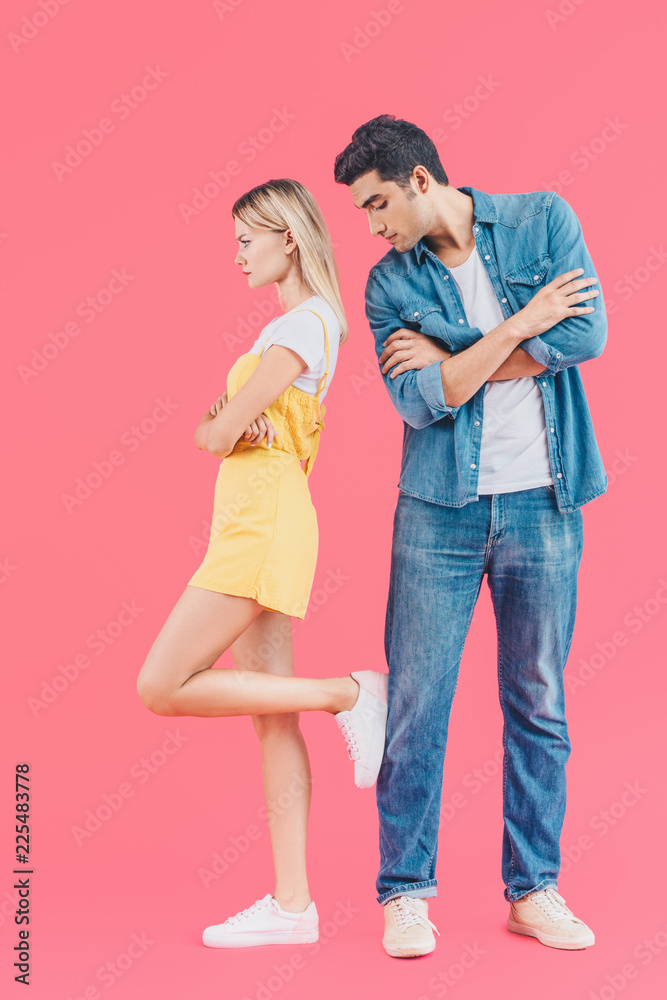 side view of angry woman standing with crossed arms and putting one leg on boyfriend while he looking down isolated on pink