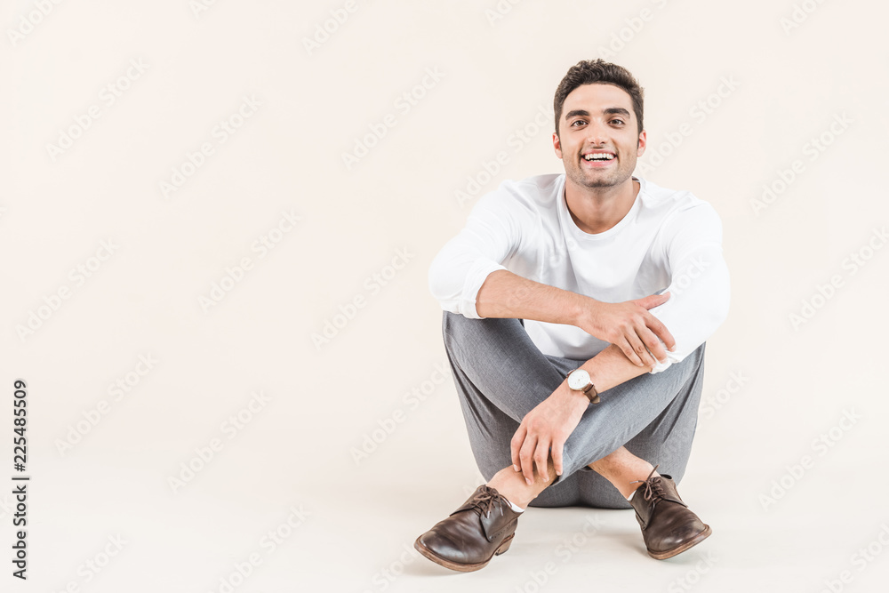 cheerful young man sitting and smiling at camera isolated on beige cheerful young man sitting and smiling at camera isolated on beige