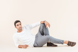 full length view of handsome young man lying and smiling at camera isolated on beige