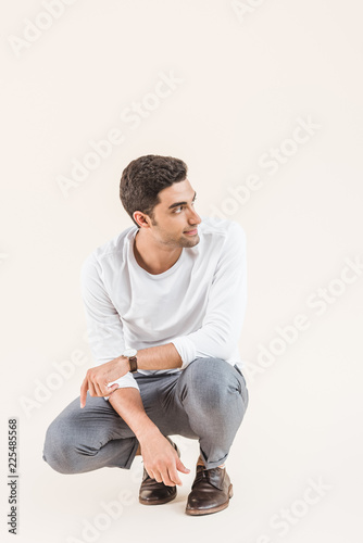 Slika na platnu handsome smiling young man crouching and looking away isolated on beige