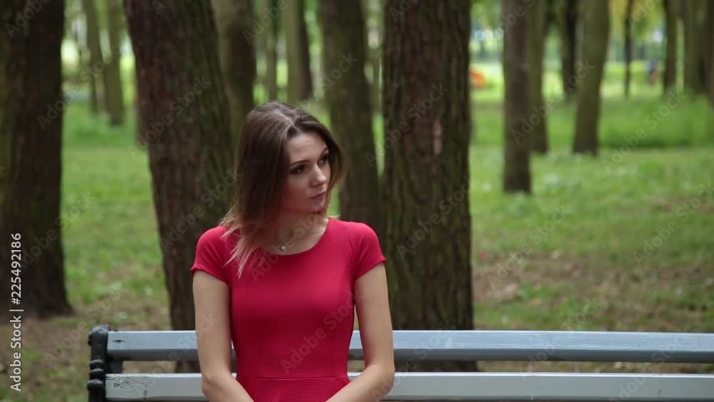 Young beautiful girl in a red dress is sitting on a bench in the park. Young beautiful girl in a red dress is sitting on a bench in the park.