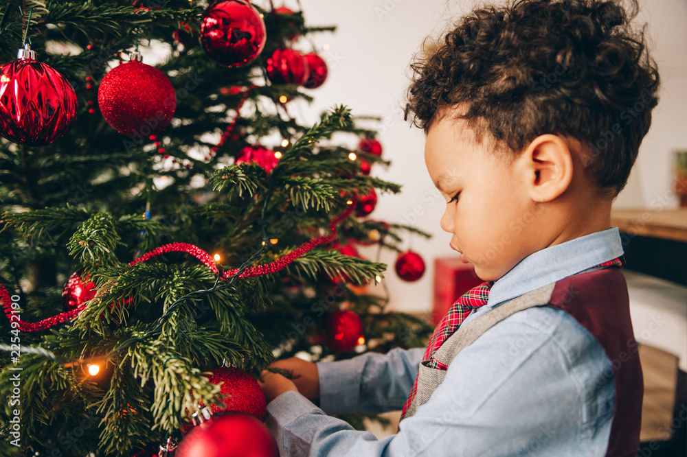 Adorable 3 year old toddler boy decorating Christmas tree Adorable 3 year old toddler boy decorating Christmas tree
