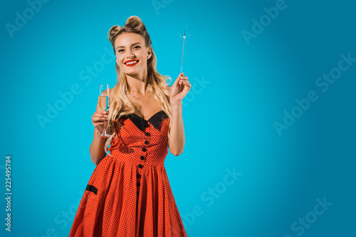 pretty pin up woman in vintage clothing with sparkler and glass of champagne on blue backdrop