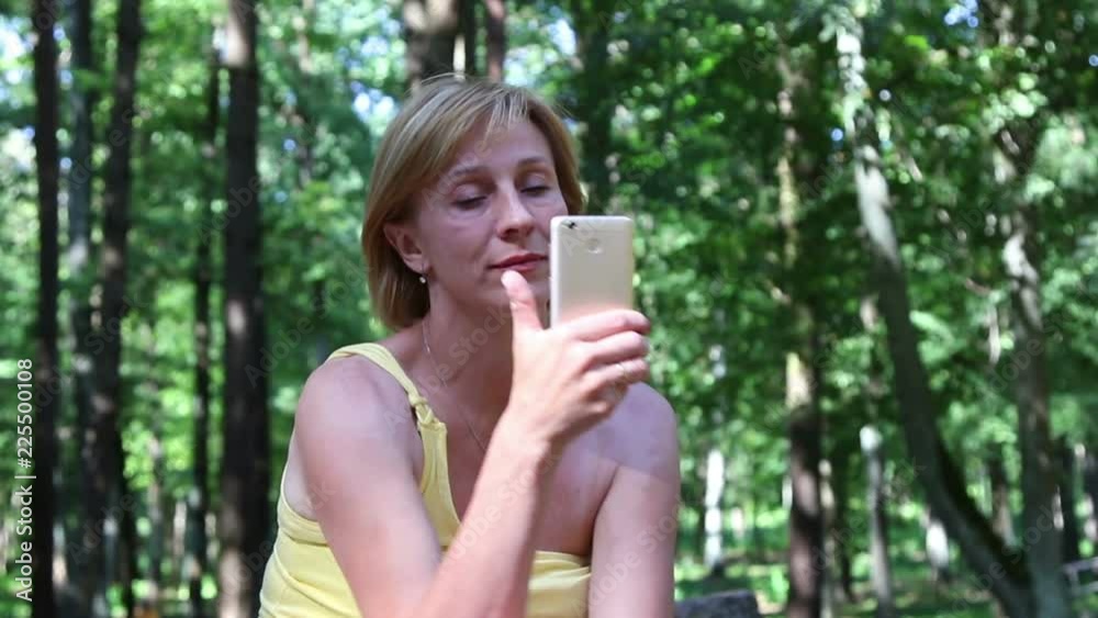 A woman makes photo using a smartphone, in a summer park.
A woman makes photo using a smartphone, in a summer park.