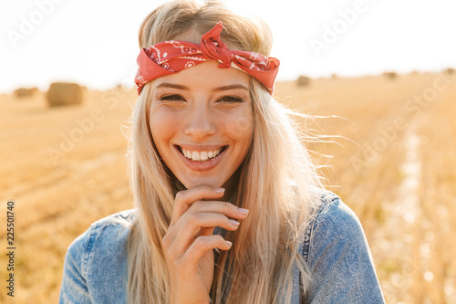 Portrait of joyous woman 20s smiling and walking through golden field, during sunny day