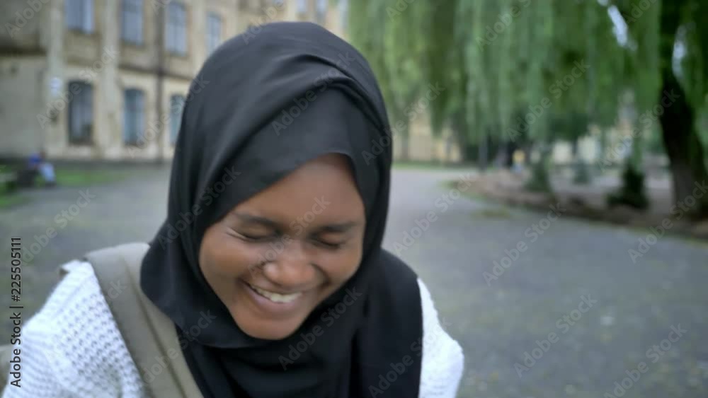 African young muslim woman in hijab laughing in camera and standing in park near university, happy and cheerful
