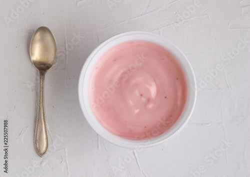 Yoghurt cup with pink strawberry yogurt on grey background with small silver spoon