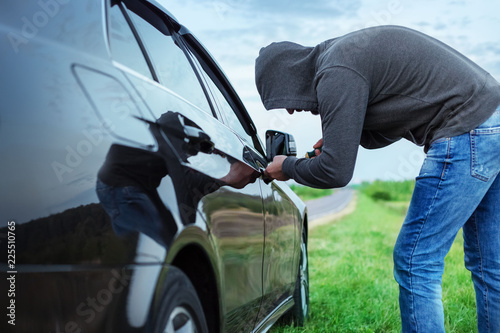 Canvas Print car thief in action, a man in a hood breaks a screwdriver car door