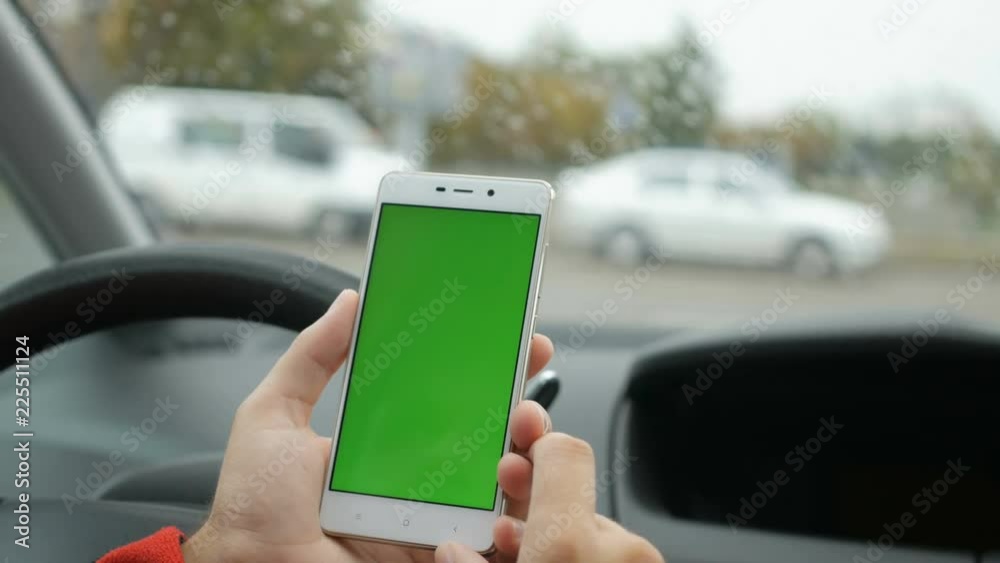 Hand holding smartphone with green blank screen in car for direction, massage, location, business. City life. Man sits in car and works on smartphone green screen closeup. Chroma key. Rainy day. Hand holding smartphone with green blank screen in car for direction, massage, location, business. City life. Man sits in car and works on smartphone green screen closeup. Chroma key. Rainy day.