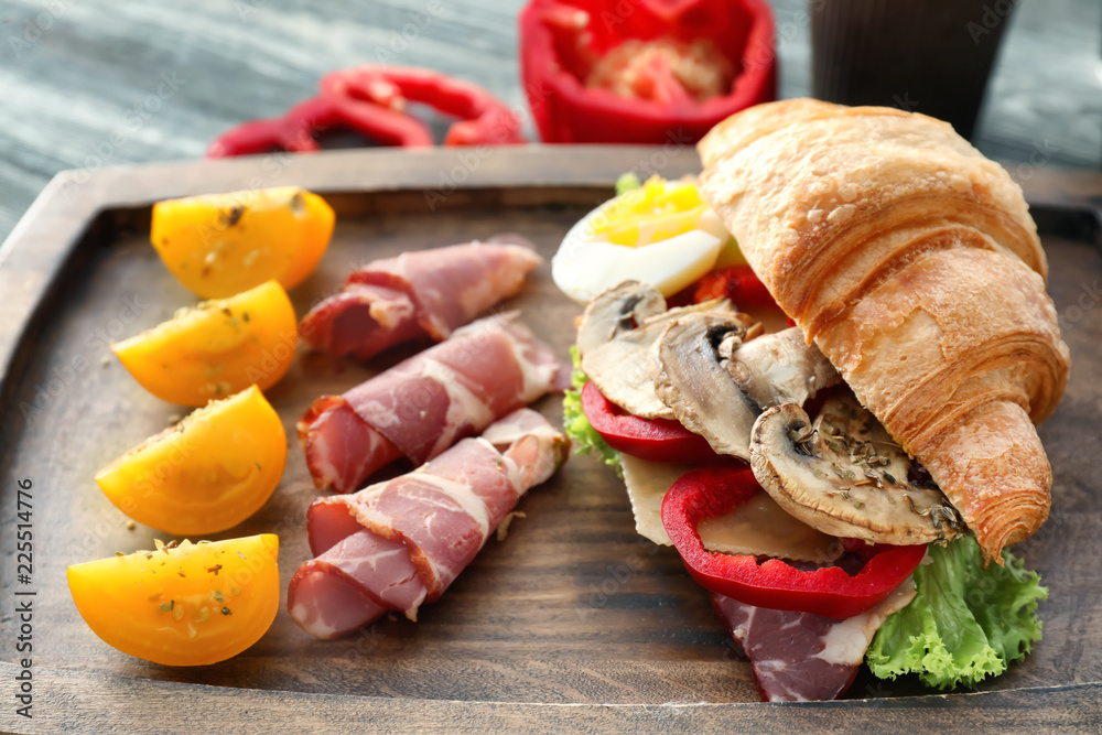 Tasty croissant sandwich with meat and tomato on wooden board, closeup Tasty croissant sandwich with meat and tomato on wooden board, closeup