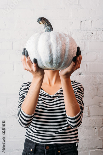 Fototapeta Naklejka Na Ścianę i Meble -  woman in striped shirt holding white painted halloween pumpkin in front of head