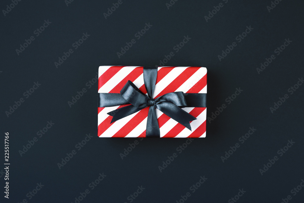 Gift box wrapped in red striped paper and tied with black bow on black background. Black friday and cyber monday concept, top view. Gift box wrapped in red striped paper and tied with black bow on black background. Black friday and cyber monday concept, top view.
