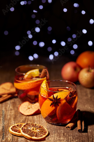 close up view of delicious hot mulled wine drinks and spices on wooden tabletop with defocused bokeh lights on background