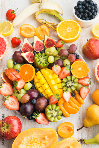 Fototapeta Naklejka Na Ścianę i Meble -  Variety of cut fruits and berries platter, strawberries blueberries, mango orange, apple, grapes, kiwis on the white wood background, copy space for text, layout, top view, selective focus
