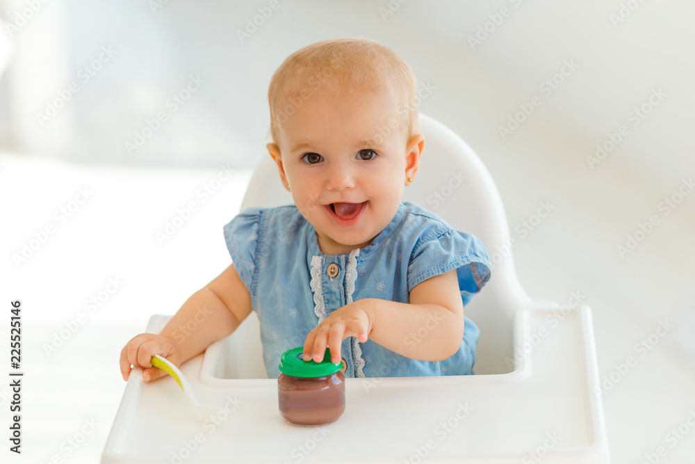 Very cute and funny baby with the spoon in hands eating kids nutrition -  fruit puree. Smiling