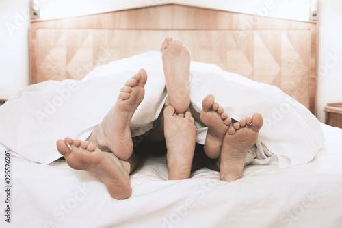 three pairs of feet lying together under bed cover in bedroom, threesome group sex concept, filtered image photo