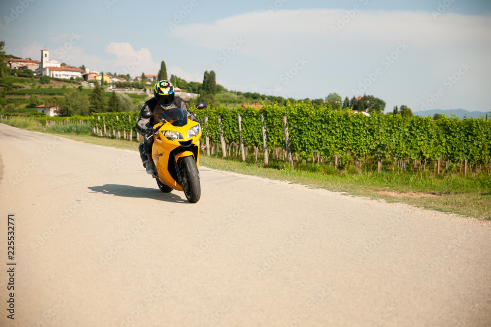 Obraz premium Man drive a motorbike on a country road with vineyards in background
